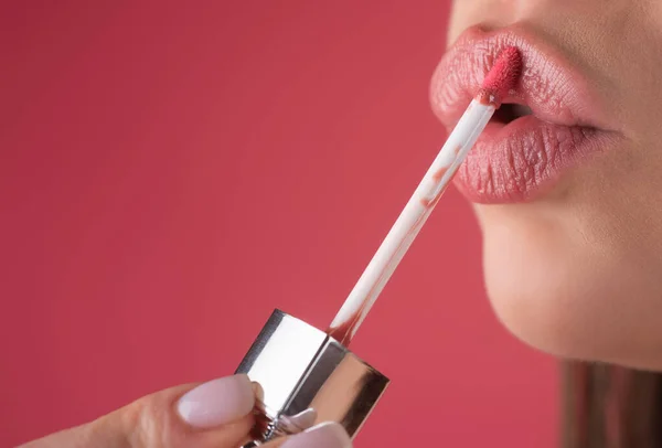 Applying lipstick, macro. Painting lips with bright lipstick, close up. Pampering, lips correction concept. Glossy lipstick on full plump lip. Woman hand applying lipstick. Lip balm