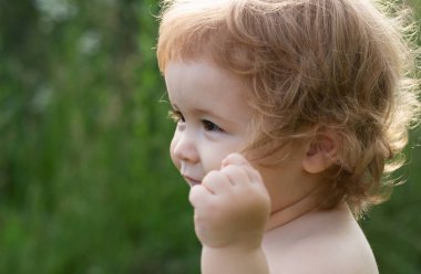 Küçük çocuk parkta oynuyor. Çim tarlasında mutlu bir bebeğin portresi. Bebek yüzlü, yakın çekim. Küçük komik çocuk portresi. Sarışın çocuk, duygusal yüz.