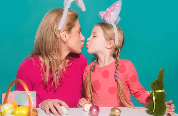Mother and daughter preparing for Easter and kissing. Cute little child girl with mom wearing bunny ears on Easter day