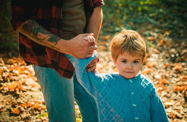 Baby boy has a good time and walk holding fathers tattooed strong hand. Happy dad and son spending time together outdoor. Family and fatherhood concept
