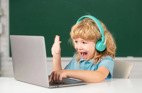 興奮した学校の少年は 驚くべき生徒はノートパソコンでヘッドフォンの書き込みを着て オーディオレッスンを聞くコンピュータを使用します ビデオコール 家庭教師との電子研究遠く — ストック写真