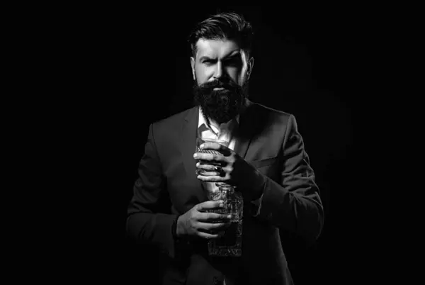 Cheerful bearded man is drinking expensive whisky. Degustation of elite alcohol. Elegant and stylish man in classical wear holding glass with wiskey in hand