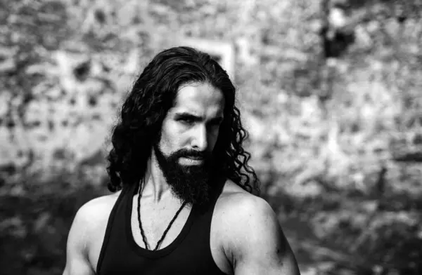 Young stylish man with determined character. Strong confident man with long wavy dark hair and beard looking at camera. Mans power and confidence concept
