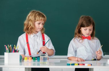 Okulda resim çizen ve resim yapan sevimli okul arkadaşları. Dost canlısı bir oğlan ve komik öğrenciler tahtaya resim çizerler. Okulda arkadaşlık.