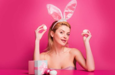 Woman with rabbit ears hold easter egg over pink background clipart