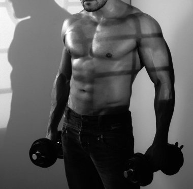 Gömleksiz vücut geliştirici halterle egzersiz yapıyor.