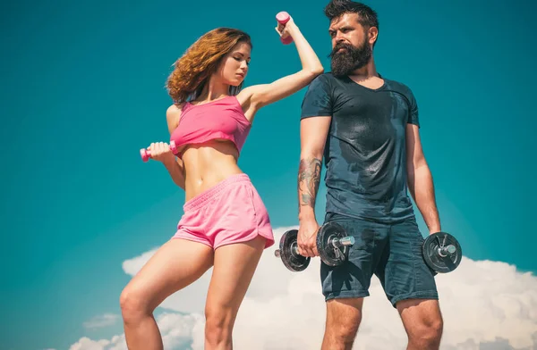 Sportive fitness couple, bearded man and sexy woman working out outdoors, sportive couple training with dumbbells