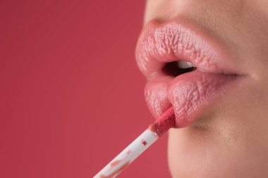 Ruj sürüyorum. Parlak rujla boyanmış dudaklar, yakın plan. Şımartma, dudak düzeltme konsepti. Dolgun dudağında parlak bir ruj. Ruj süren kadın eli