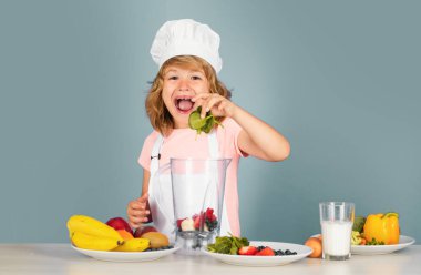 Heyecanlı komik aşçı. Çocuk fırın üniforması giyiyor ve şapka takıyor ıspanak mutfakta sebze hazırlıyor, stüdyo portresi yapıyor. Aşçılık, aşçılık ve çocuk maması konsepti.