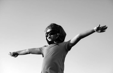 Pilot gözlüklü ve kasklı mutlu çocuk mavi gökyüzü arka planına karşı oynuyor. Güneşli bir yaz gününde gökyüzünde yürüyen sevimli bir çocuk. Çocuklar seyahat hayali kurar.