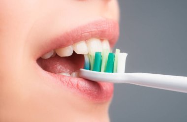 Diş fırçası ve diş fırçasıyla yakın plan ağız. Diş fırçası tutan sağlıklı dişleri olan gülümseyen genç bir kadın. Diş sağlığı kliniği. Genç bir kadının yakın çekimi dişlerini fırçalıyor.
