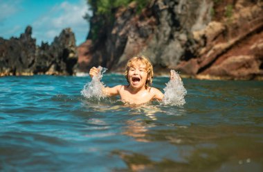 Okyanus suyunda oynayan bir çocuk. Çocuk deniz dalgalarında zıplıyor. Çocuklar plajda tatil yapıyor. Küçük heyecanlı çocuk yaz tatilinde yüzüyor.