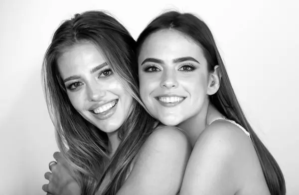 Women face of two happy smiling sexy girls, close-up. Beauty portrait of young happy beautiful blonde and brunette women. Two women friends laughing with a perfect white teet