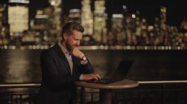Night City 'de çok çalışan bir iş adamı. Çok çalışan adam dışarıda dizüstü bilgisayarda çalışıyor. Gece sokağındaki iş adamı. Çok çalışan bir ofis çalışanı. İşadamı geceleri laptopunu kullanarak dışarıda çok çalışıyor.