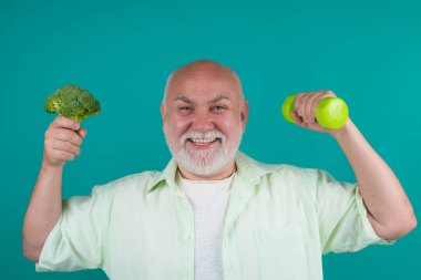 Sağlıklı bir son sınıf öğrencisi. Formda yaşlı insanlar için sağlıklı yiyecekler. Güçlü, olgun bir adam. Büyükbaba, dambıl ve brokoli tut. Sağlıklı yaşlı son sınıf, stüdyo. Sağlıklı beslenme. Yıllanmış diyet. Güçlü bir sağlık uzmanı