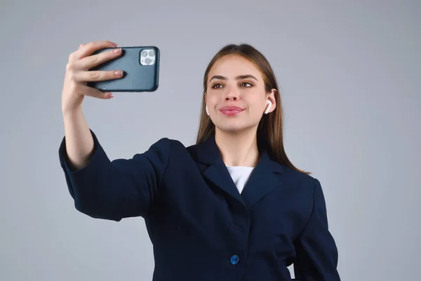 Business woman using phone and making video call. Girl make selfie with smart phone. Businesswoman with phone in studio. Young Woman in suit hold phone. Portrait of student having video-call