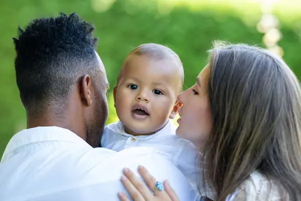 Happy multiethnic parents and amazed mixed race baby. Mixed race family outdoor portrait. Happy biracial family hug baby child. Beautiful diverse family. Multiracial family have fun together