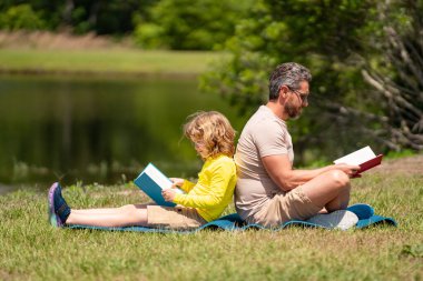 Baba oğul parkta kitap okuyorlar, insan çocuğu bilgiye, aile eğitimine teşvik ediyor. Baba ve çocuk dışarıda birlikte kitap okurlar. Çocuk kitabıyla parkta yaz doğası hakkında mutlu ebeveynler okuması