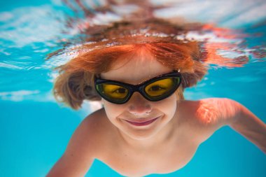 Yaz çocuğu Aquapark 'ta rahatla. Yaz tatili. Küçük çocuk havuzda su altında yüzüyor. Yaz gözlüğü takan çocuk havuz başında suyun altında yüzer. Su altı fotoğrafı.