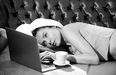 Kız dinleniyor, dizüstü bilgisayarla sohbet ediyor, lüks yatak odasında rahat bir kanepede kahve içiyor. Çekici seksi kadın otel odasında bornoz ve havlu giyerek rahatlıyor.