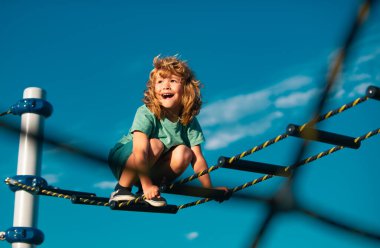 Sevimli çocuk oyun parkında merdivenleri tırmanıyor. Çocuk mavi gökyüzüne karşı merdiveni tırmanır. Metin için alanı kopyala