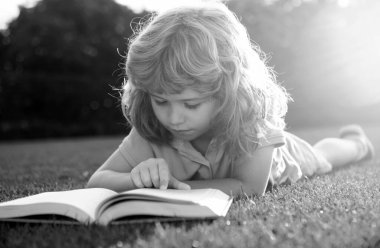 Zeki zeki çocuklar. Çocuk bahçede faiz kitabı okuyor. Yaz eğlencesi. Çimlerin üzerinde uzanmış çocuk kitabı okuyor.