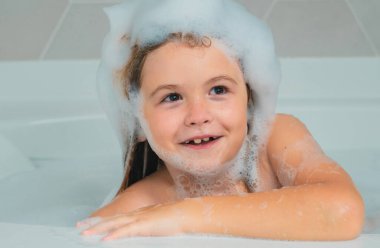 Mutfak lavabosunda bol köpüklü banyo yapan kafası köpüklü mutlu çocuk.