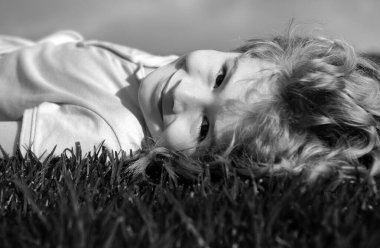 Yeşil çimlerin üzerinde uzanmış hayal kuran gülümseyen küçük bir çocuğun portresi. Doğanın tadını çıkaran sevimli bir çocuk. Sağlıklı kaygısız çocuk yaz parkında çimlerin üzerinde oynuyor.