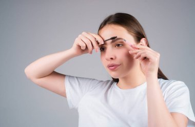 Güzellik salonunda fırçayla kaşlarını tarıyor. Uzun kirpikli ve kalın kaşlı bir kadın. Doğal güzellik kaşları. Doğal makyajlı genç bir kız.