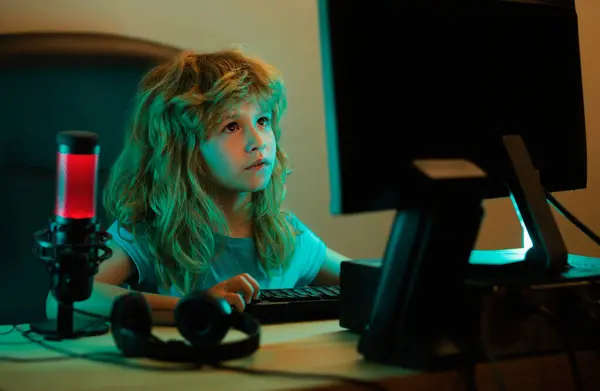 Child playing computer games or studying on pc computer. Kid gamer on night neon lighting. Little hacker, young programmer