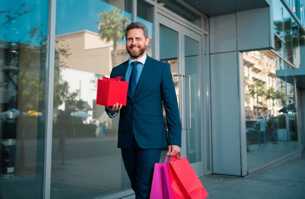 Businessman walking. Handsome man doing shopping in the city. Portrait of business man in suit with shopping bags
