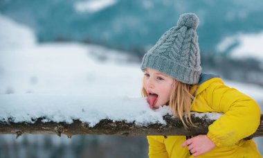 Dışarıda kar yiyen tatlı küçük bir kış kızı. Heyecanlı Noel çocukları tatili. Çocuklar soğuk algınlığı ve grip. Çocuk diliyle kar yalıyor.