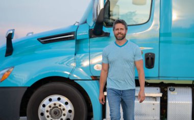 Kamyonun yanında erkek sürücü var. Kamyonetin yanındaki tişörtlü adam. Yakışıklı, orta yaşlı kamyoncu kamyoncu adam. Yarı karavan, yarı kamyon. Kamyonun önünde poz veren yakışıklı bir adam.