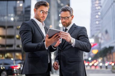 Gece vakti iş adamı Ney York. İki iş adamı dışarıda tablet dizüstü bilgisayar kullanıyor. İşadamları gece şehrinde iş başarısı için tablet arıyorlar. Gece işi.