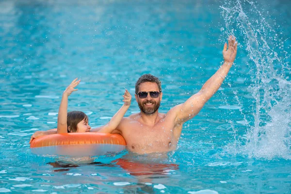 Father and son swimming in pool, summer family weekeng. Father and son splash water in pool on summer family holiday. Dad and child relaxing in pool water. Child with dad swimming in pool