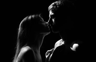 Birbirine aşık romantik bir çift birbirine bakar, sarılır ve siyah arka planda öpüşür.