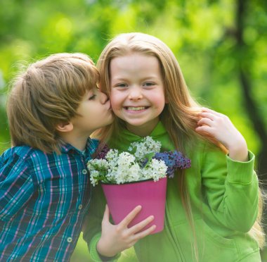 Two little children hug and kiss each other in summer garden. Kids couple in love. Friendship and childhood. Little girl kissing little boy outdoors in park