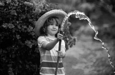 Küçük mutlu çocuk ev bahçesinde eğleniyor. Çocuk bahçe hortumunu tutuyor. Hasat zamanı arka bahçede çocuklar için açık hava oyunları..