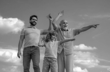 Men generation: grandfather father son and grandson playing with toy paper plane outdoor on sky. Boy dreams of becoming a pilot