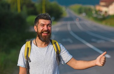 Otomatik bilgisayarla seyahat, yaz tatili. Otomatik seyahat. Katı yüzlü ve sakallı bir adam arka planda otostop çekerek seyahat ediyor.