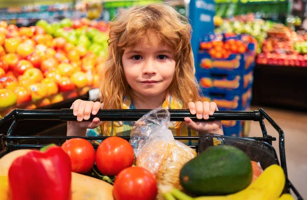 Child in supermarket buying fruit. Kid grocery shopping. Kid with cart choosing fresh vegetables in local store. Little child choosing fresh vegetables in a food store