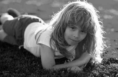 Yaz parkında çimlerin üzerinde yatan küçük mutlu çocuk. Yeşil çimlerin üzerinde uzanmış gülümseyen bir çocuğun portresi. Bahçedeki çayırda küçük şirin bir çocuk.