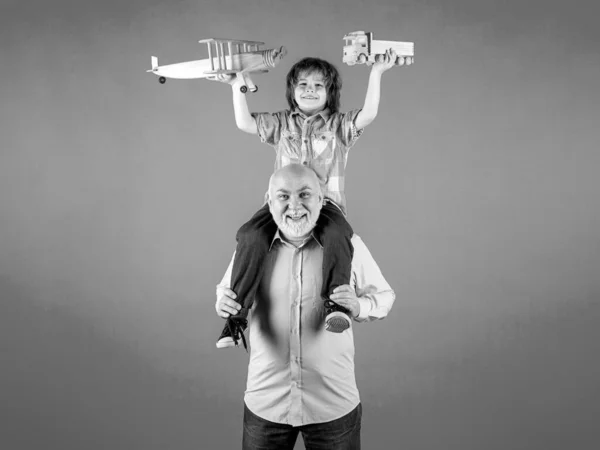 Child boy and grandfather playing piggyback ride with plane and wooden toy truck. Men generation granddad and grandchild. Elderly old relative with child