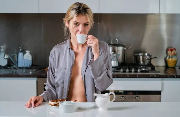 Sensual girl with undressed pajama enjoy coffee. Sexy woman sitting in the kitchen in the morning and drinking coffee. Sensual housewife