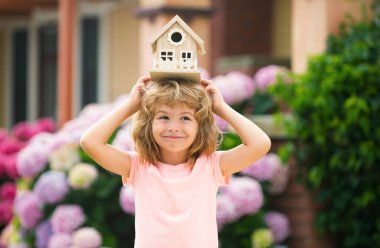 Komik çocuk oyuncak evi tutuyor. Çocuk yeni bir rüya evi yapıyor. Aile rüyası. Kafasında oyuncak tahta evi olan sevimli bir çocuk.