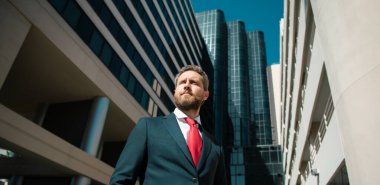 Yönetici işadamı. Modern ofis yakınlarında takım elbiseli bir CEO portresi. Şirket binasının önünde duran mutlu lider.