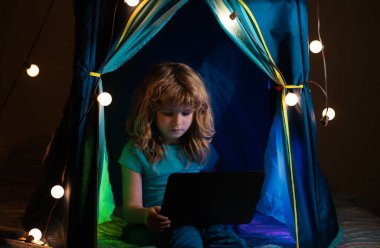 Çocuk evde çadırda oturup dizüstü bilgisayarla oynuyor. Çocuklar için sosyal medya