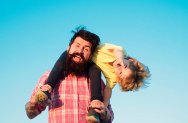 Heyecanlı oğul babasına sarılıyor. Babalar Günü. Mutlu gülümseyen babanın portresi oğluna omuzlarına bindirirken