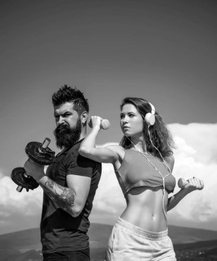 Güçlü erkek ve seksi kadın arka planda dambıllarla çalışıyor. Dambıl ağırlıklarıyla çalışan çift. Çekici kadın ve yakışıklı kaslı adam dışarıda antrenman yapıyor.