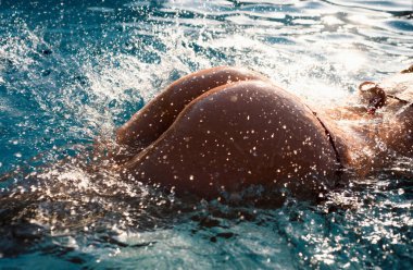 Sexy buttocks in pool closeup, summer journey, sensual woman with hot natural butt relax in water. Wet body, ass in sexy bikini. Seduction and pleasure model. Luxury passion buttocks